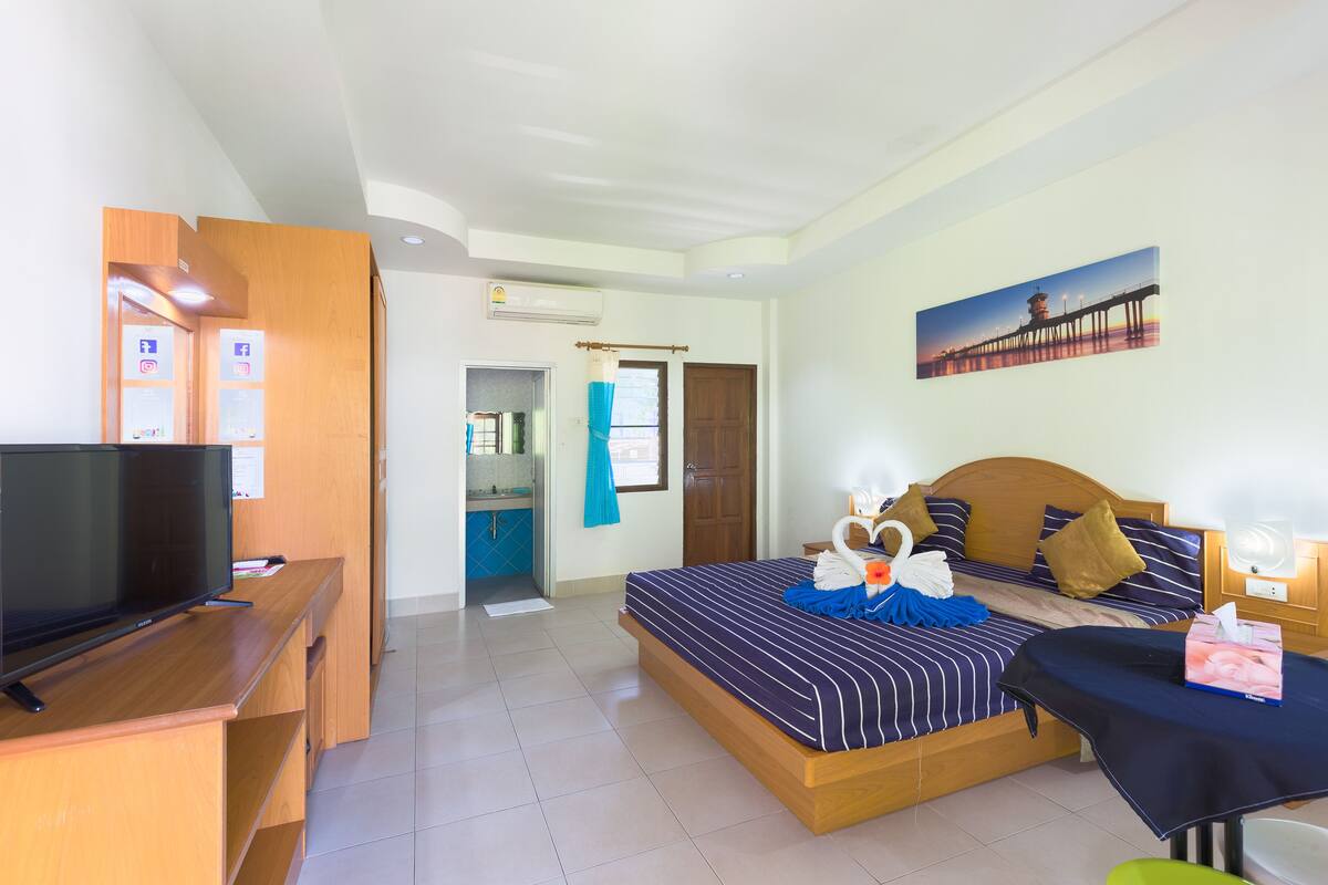 A hotel room with a bed, a desk with a TV, a bathroom, and a painting on the wall.