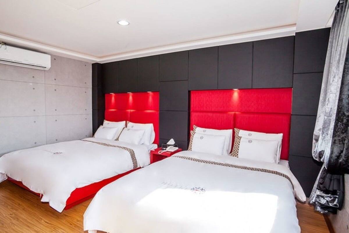 A hotel room with two beds, each with red headboards and white bedding.