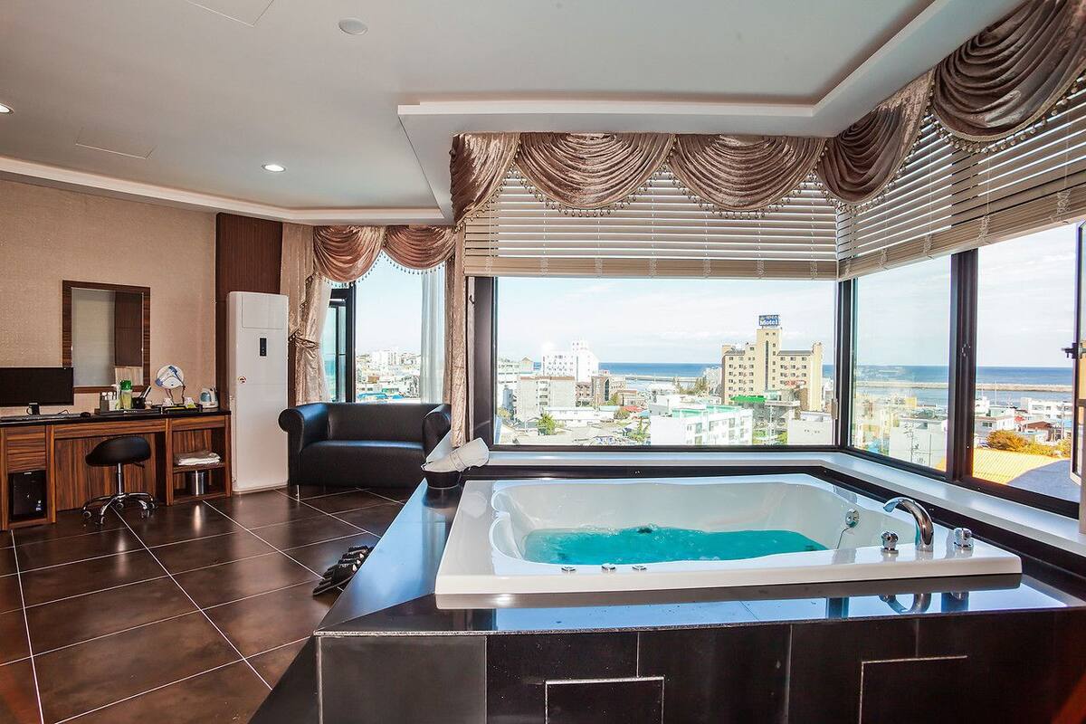 A modern bathroom with a large bathtub, a vanity with a mirror, and a view of the cityscape through large windows.