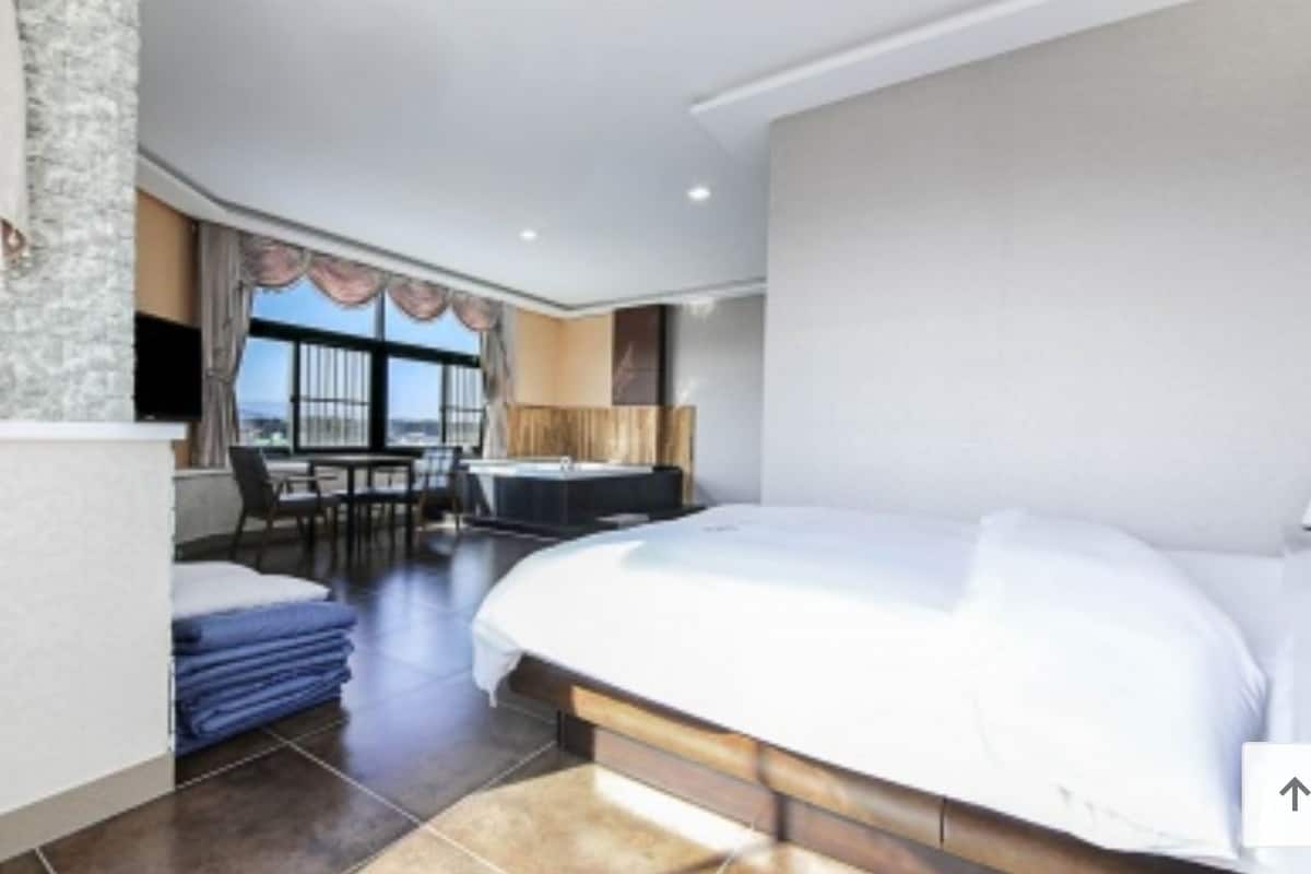 A hotel room with a bed, a desk, a chair, a small table, and a view of the outside.