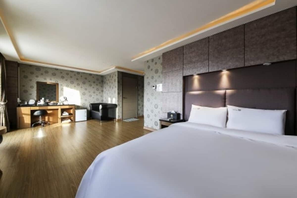 A modern hotel room with a large bed, a desk, and a wardrobe.