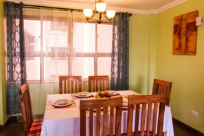 Comedor con una mesa dispuesta para seis personas, sillas de madera, una araña y un cuadro en la pared.