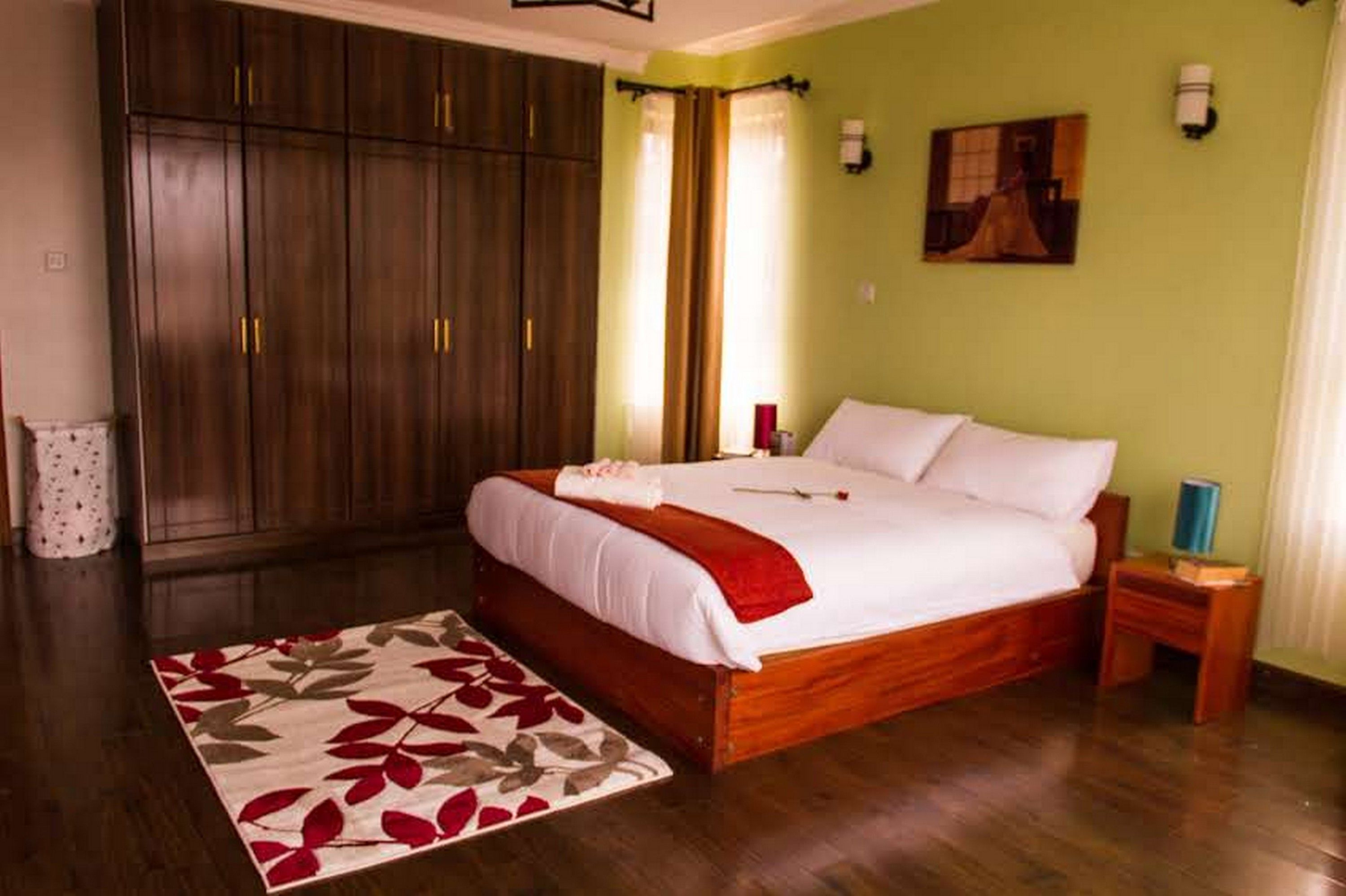 A bedroom with a large bed, wooden wardrobe, and a floral rug.