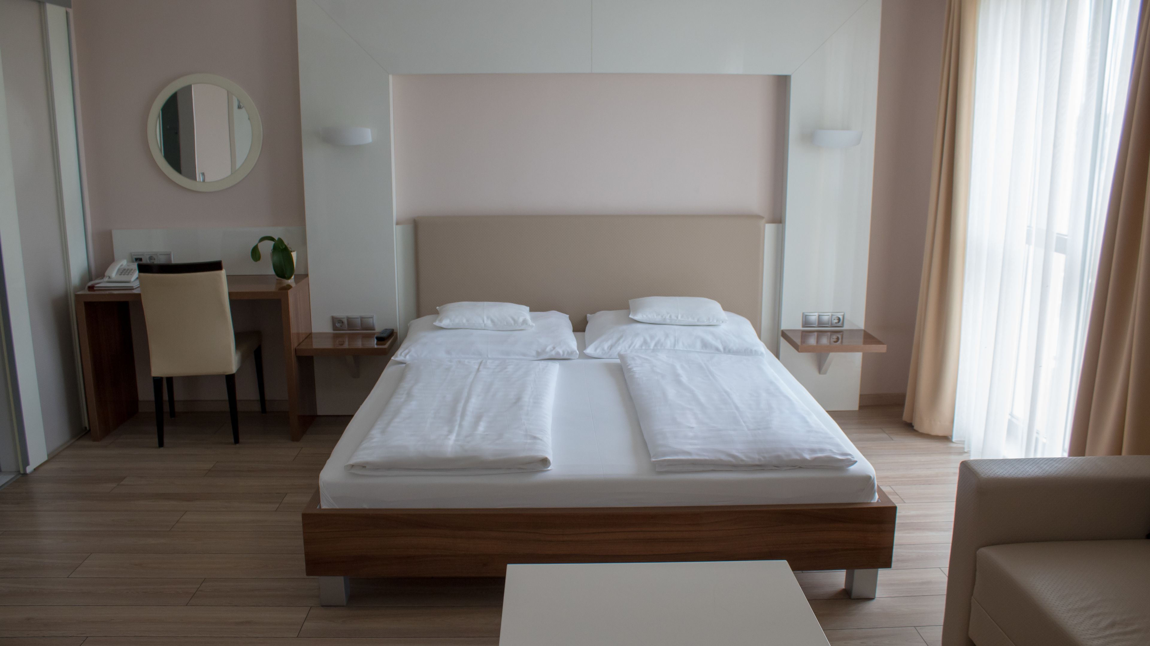A hotel room with a large bed, a desk, a chair, and a small table.
