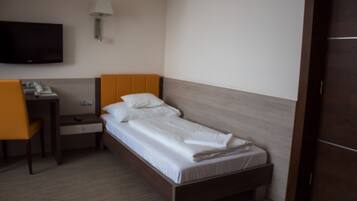 A single bed with white linens, a wooden headboard, a bedside table with a lamp, and a chair.