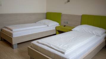 Dos camas individuales con cabeceros de madera y ropa de cama blanca, una mesita de noche verde y un interruptor de luz en la pared.