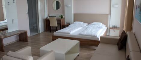 A modern hotel room with a large bed, a desk, a chair, and a sofa.