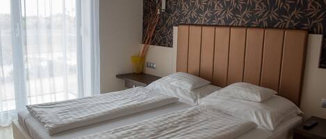 A double bed with a headboard, a bedside table with a lamp, and a window with sheer curtains.