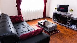 Ein modernes Wohnzimmer mit einer schwarzen Ledersofa, einem Glastisch und einem Flachbildfernseher auf einem Holzboden.