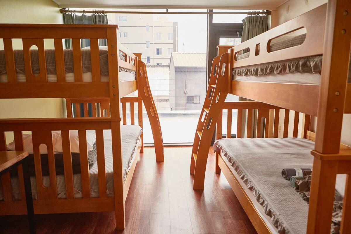Une chambre de dortoir avec des lits superposés et une fenêtre donnant sur un paysage urbain.