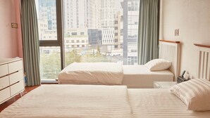 Une chambre d’hôtel avec deux lits, une commode, une fenêtre avec des rideaux et une vue sur les bâtiments de la ville.