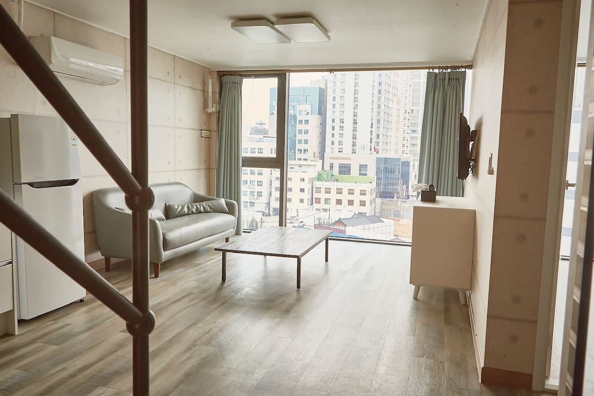 Un salon moderne avec un canapé, une table basse et une vue sur le paysage urbain, visible à travers de grandes fenêtres.