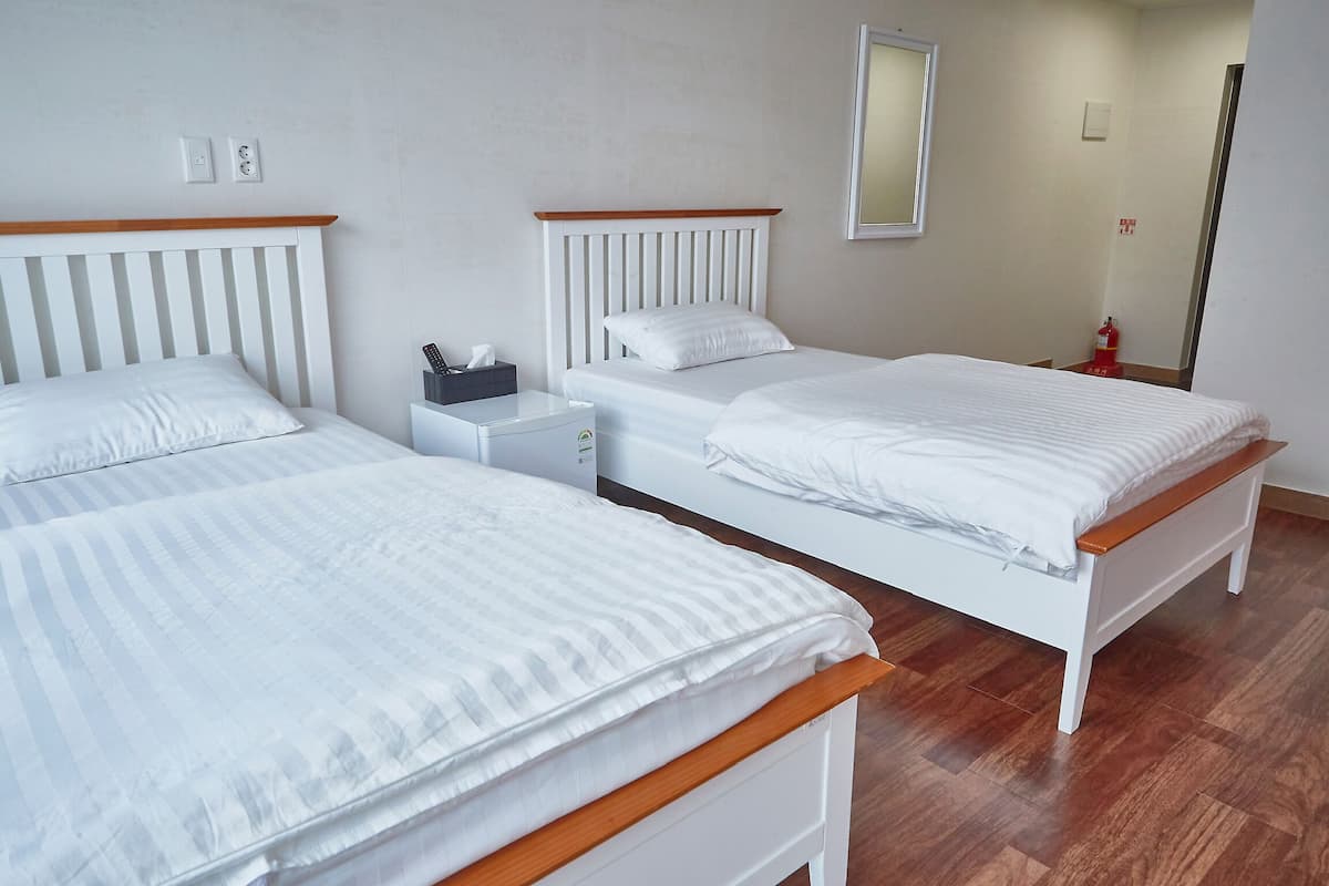 Une chambre d’hôtel avec deux lits simples, une table de chevet, une commode, un miroir et un extincteur.