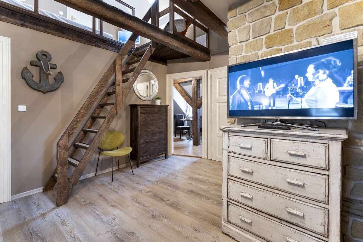 Ein Zimmer mit einer Holztreppe, einem Fernseher und einem Schminktisch.