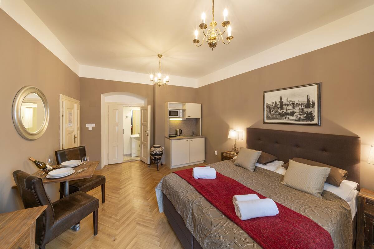 Ein Hotelzimmer mit Bett, Esstisch, Stühlen, einer Kristallleuchtre, einer Mikrowelle und einem gerahmten Bild an der Wand.