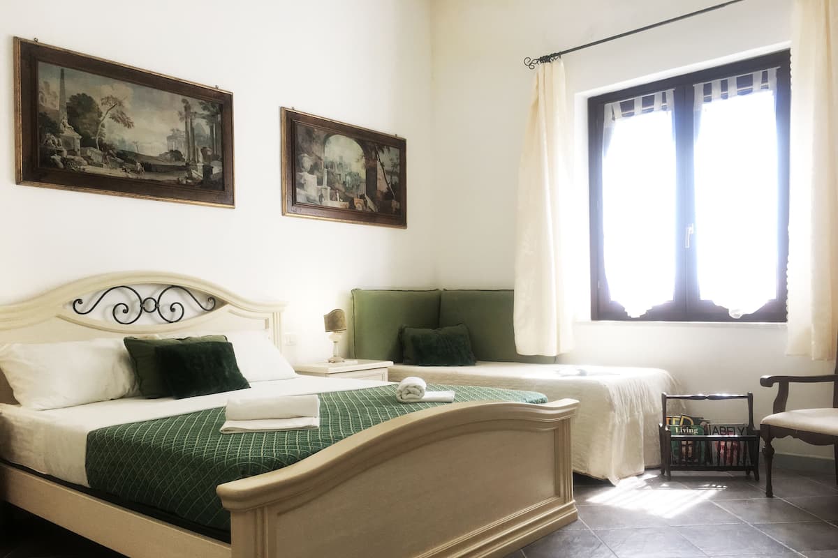 Een slaapkamer met een bed, twee nachtkastjes, een stoel en een raam met gordijnen.