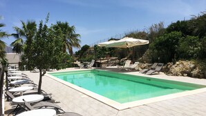 A swimming pool with lounge chairs and tables, surrounded by greenery and a clear sky. - Villa Panoramica Sul Mare (Valderice)