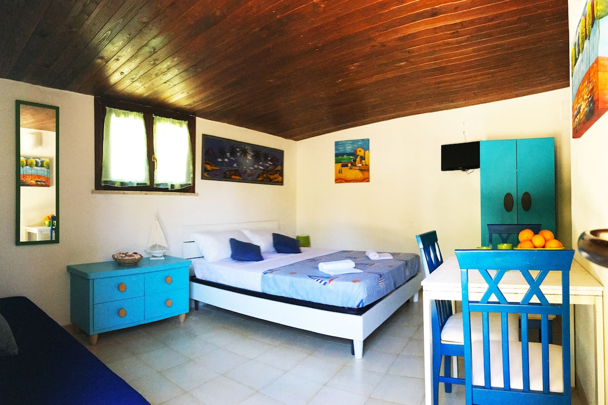Een slaapkamer met een bed, een kapstok, een stoel en een tafel met sinaasappels.