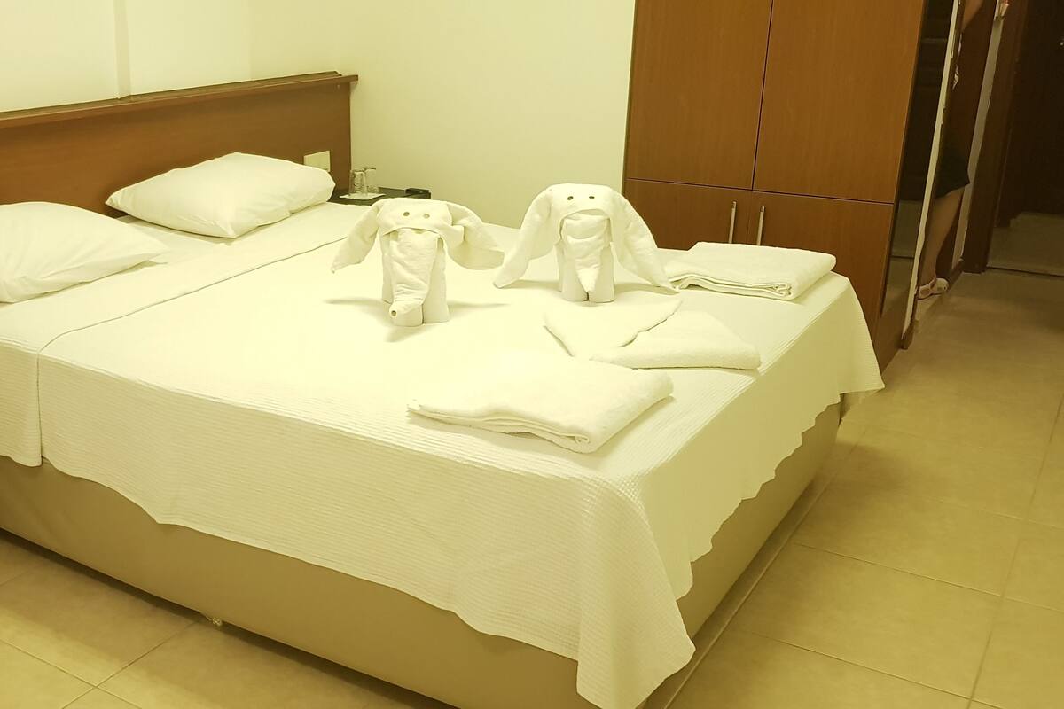 A hotel room with a bed, pillows, a nightstand, and a wardrobe.