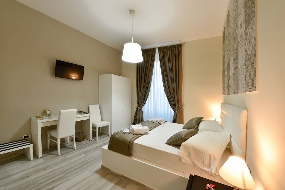 A hotel room with a bed, desk, chair, and a television on the wall.