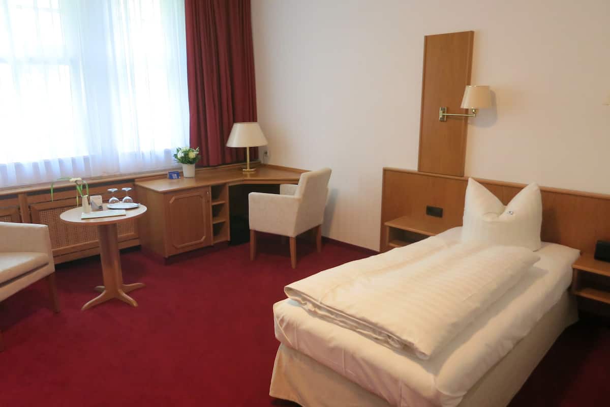 A hotel room with a bed, a desk, a chair, a small table, and a mirror.