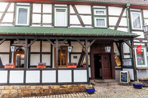 A traditional half-timbered building with a green roof, multiple windows, and potted plants on the ground level. - Hotel Schwalenberger Malkasten (Schieder-Schwalenberg)