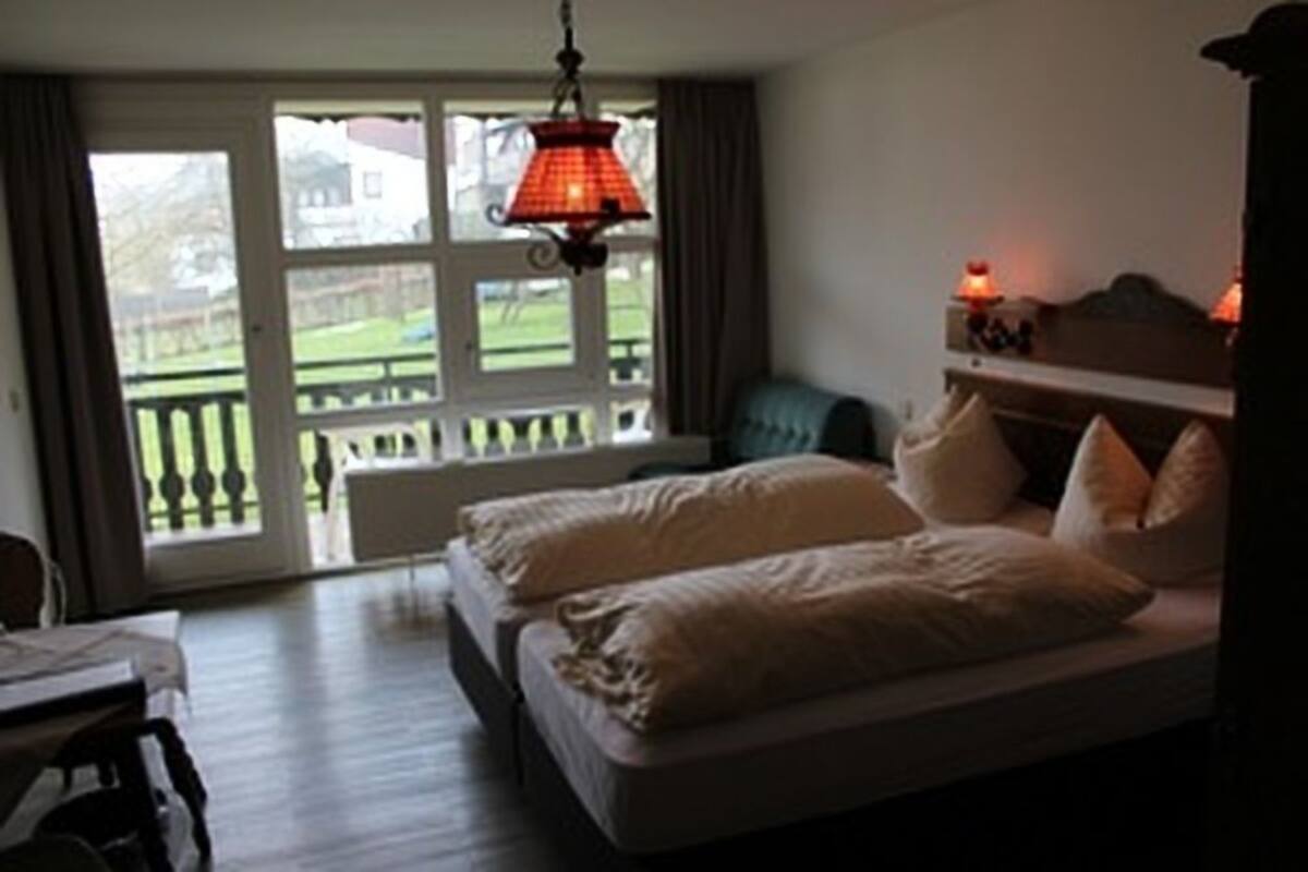 Ein Schlafzimmer mit zwei Betten, einem Fenster mit Gartenblick und einer Hängelampe.