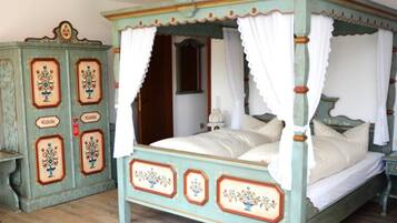 A four-poster bed with a canopy, a vintage-style dresser with floral decorations, and a small bedside table.