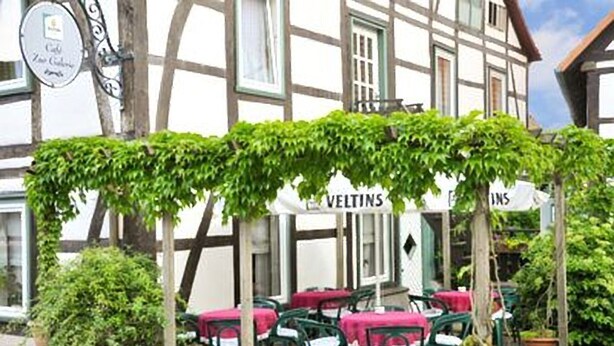 A traditional half-timbered building with a covered outdoor seating area and a sign reading "VELTINS." - Hotel Schwalenberger Malkasten (Schieder-Schwalenberg)