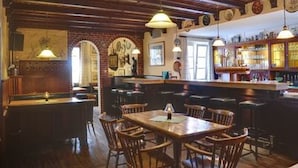 A bar with wooden beams and a brick wall, wooden tables and chairs, and hanging pendant lights. - Hotel Schwalenberger Malkasten (Schieder-Schwalenberg)