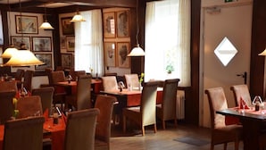 A restaurant with multiple tables and chairs, framed artwork on the walls, and hanging lamps. - Hotel Schwalenberger Malkasten (Schieder-Schwalenberg)