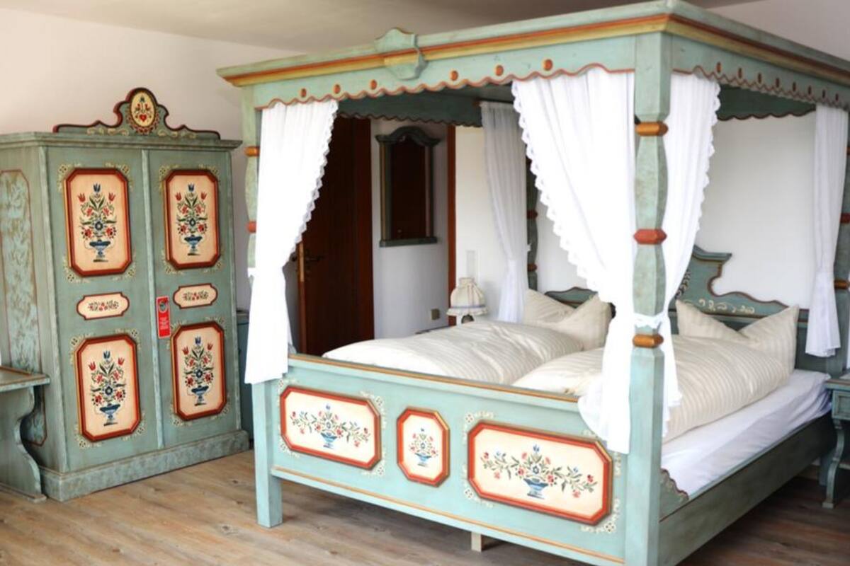 Ein Bett mit Baldachin, eine Kommode im Vintage-Stil mit floralen Verzierungen und ein Holzboden.