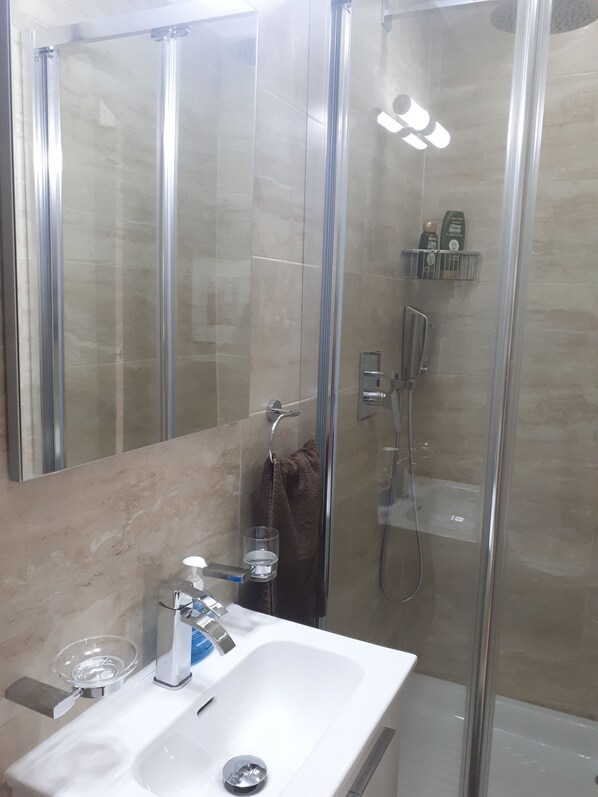 A modern bathroom with a glass-enclosed shower, a white sink, and a mirror.
