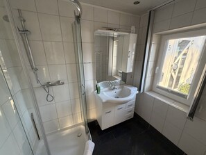 A bathroom with a glass shower enclosure, a sink with a mirror, and a window with a view. - Hotel Rühen 24-hour check-in, free parking, guest kitchen (Rühen)
