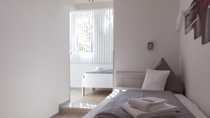 A modern bedroom with a bed, a bedside table, and a window with blinds. - Hotel Rühen 24-hour check-in, free parking, guest kitchen (Rühen)