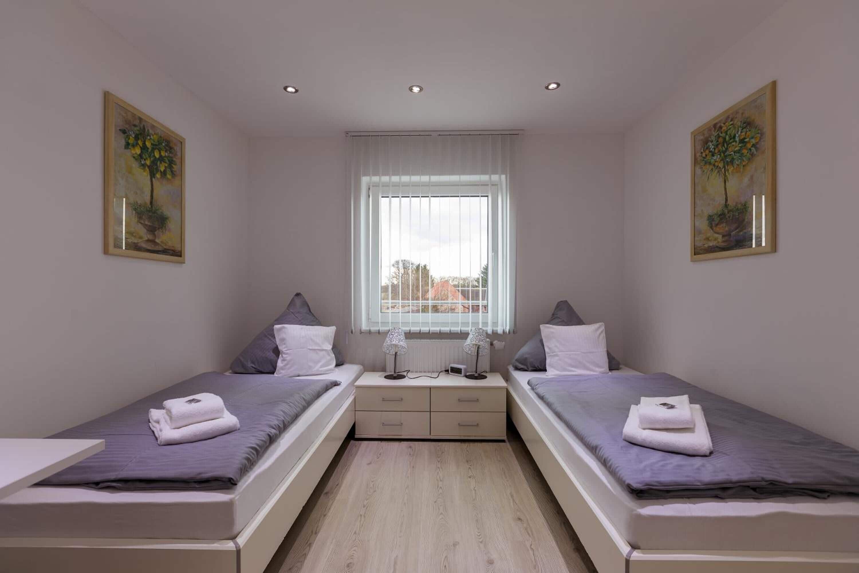 A twin bedroom with two beds, a window, and artwork on the walls.