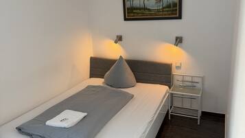 A modern bedroom with a bed, bedside tables, an air conditioner, and a framed landscape painting.