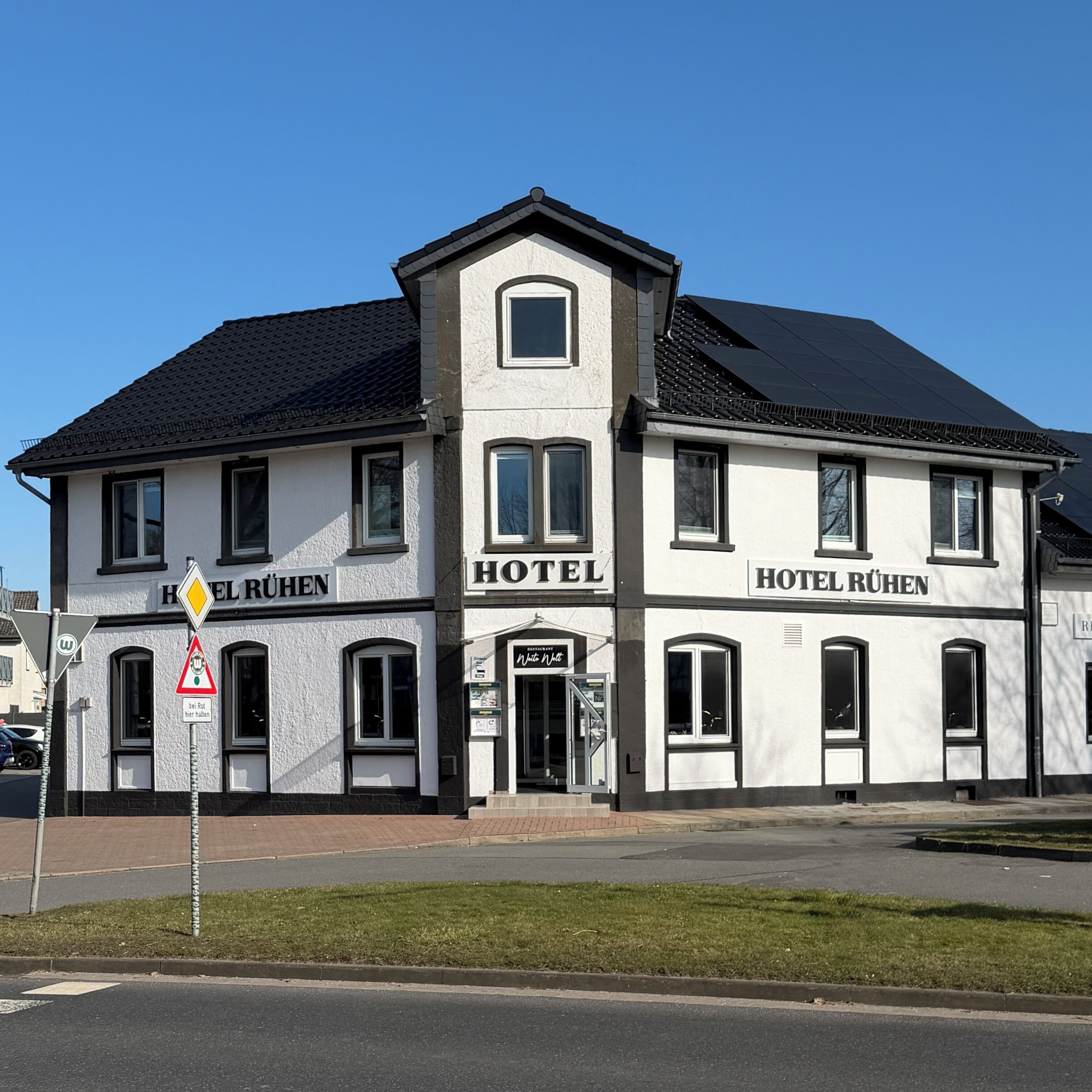Ett hotell i två våningar med skylten ”HOTEL RÜHEN”, en väl synlig entré och en parkeringsplats framför.