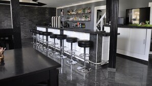A modern bar area with a long counter, multiple stools, and a variety of liquor bottles on shelves. - Hotel Rühen 24-hour check-in, free parking, guest kitchen (Rühen)