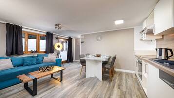 A modern living room with a sofa, coffee table, and dining table. There is a kitchen area with cabinets and appliances.
