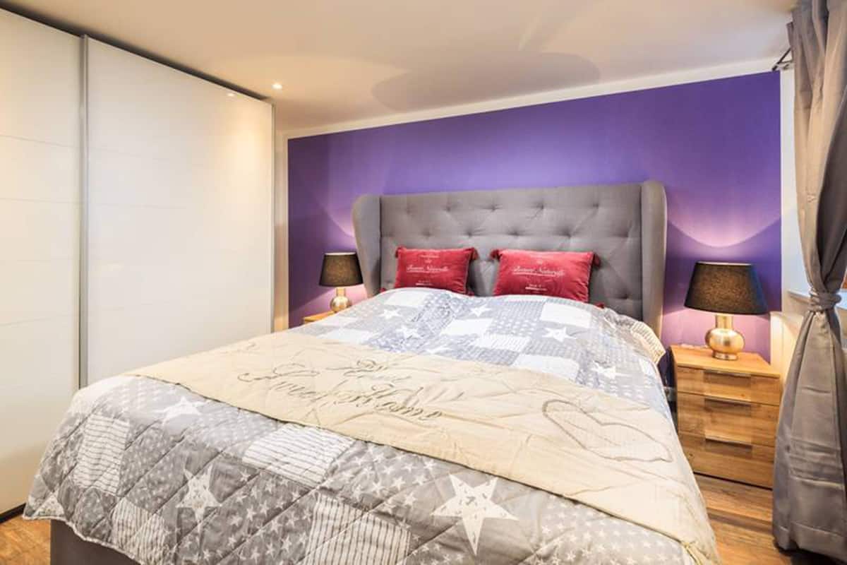 A bedroom with a large bed, purple walls, and two bedside tables with lamps.