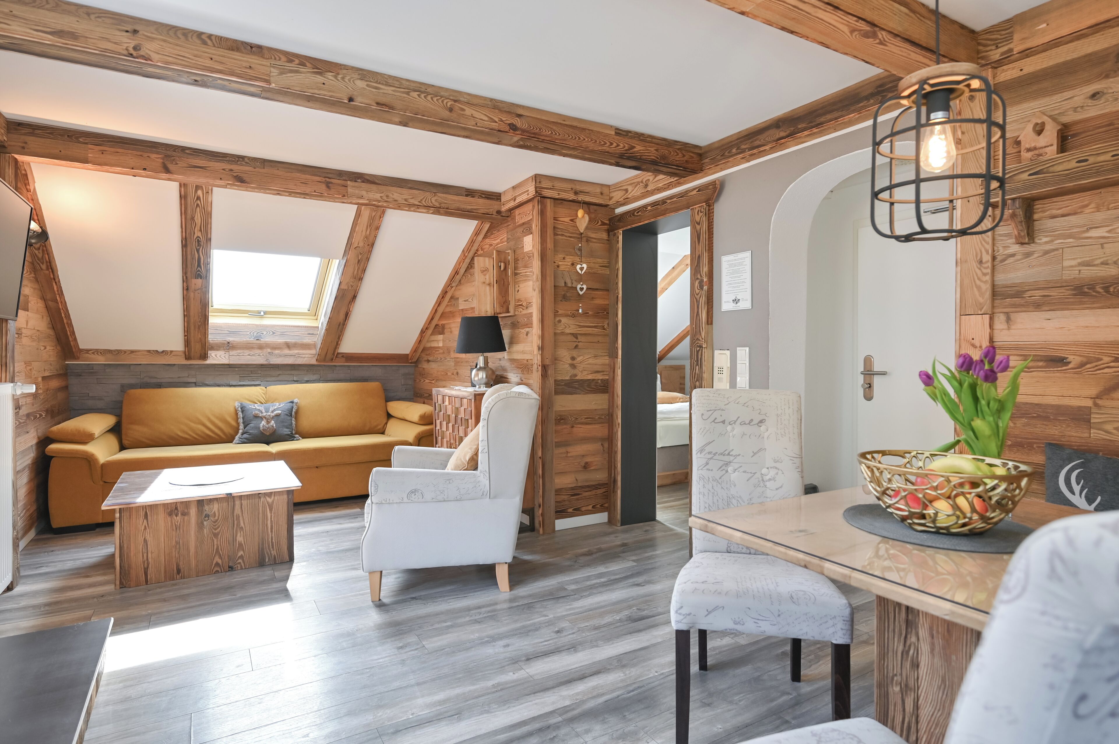 Un acogedor loft con vigas de madera a la vista, tragaluces, un sofá, una mesa de comedor y una silla.