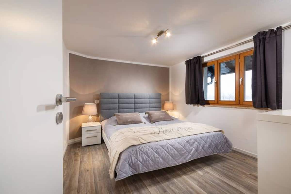 A bedroom with a bed, bedside tables, a window with curtains, and a ceiling light.