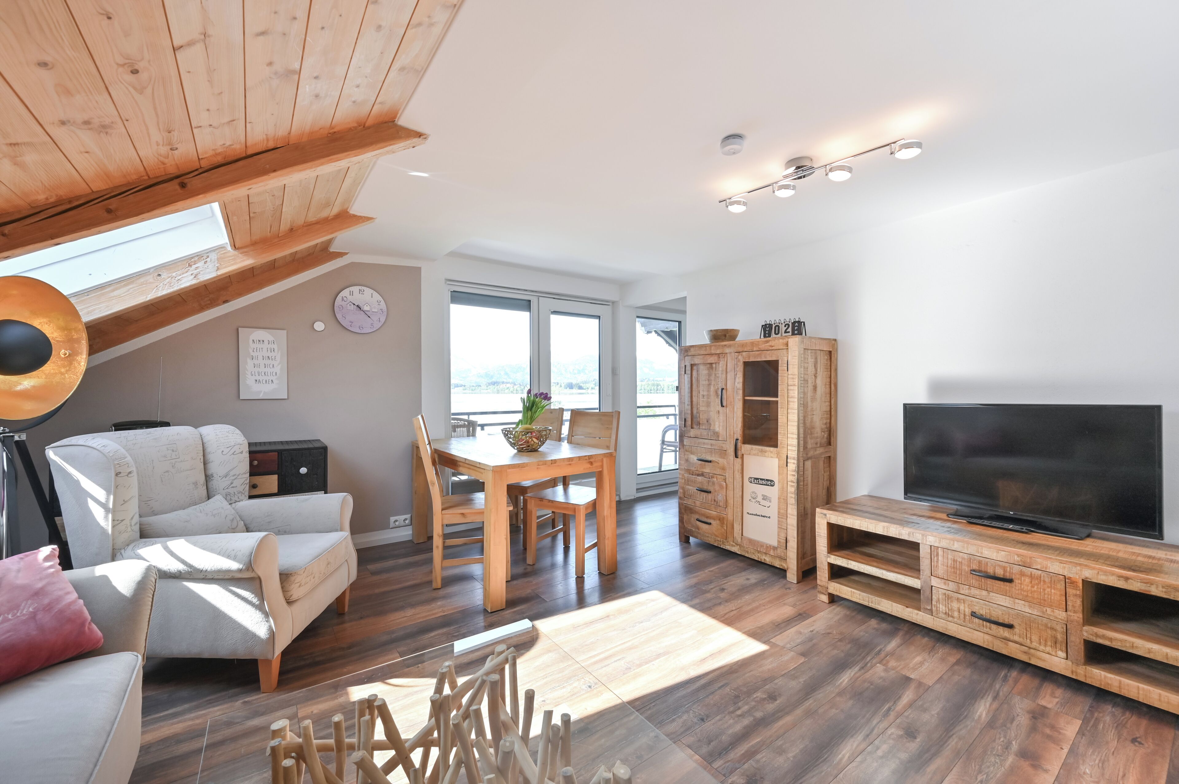 Una sala de estar moderna con techo de madera, comedor, mueble para televisión y ventana grande con vista a la ciudad.