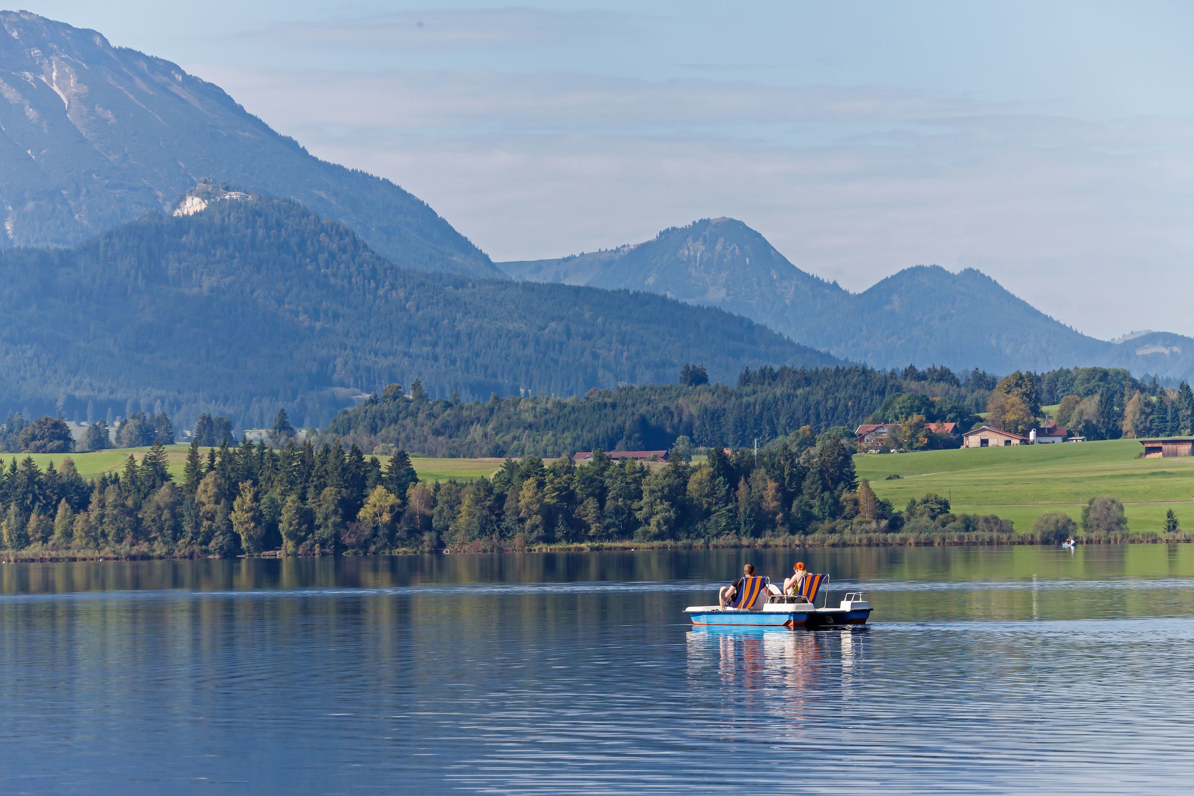 A lake with a boat carrying passengers, surrounded by mountains and a green landscape.