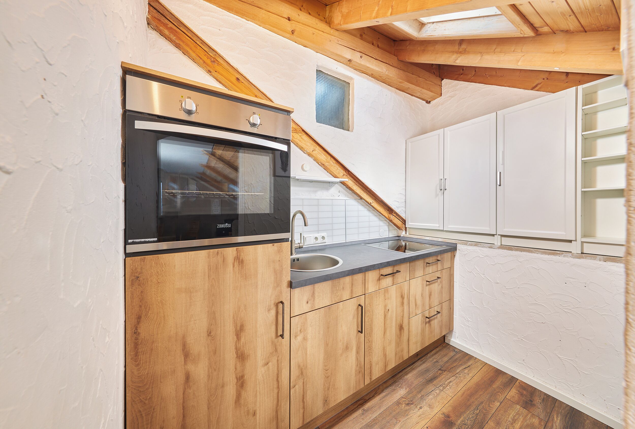 Een keuken met houten kastjes, een roestvrijstalen oven en een raam boven de gootsteen.