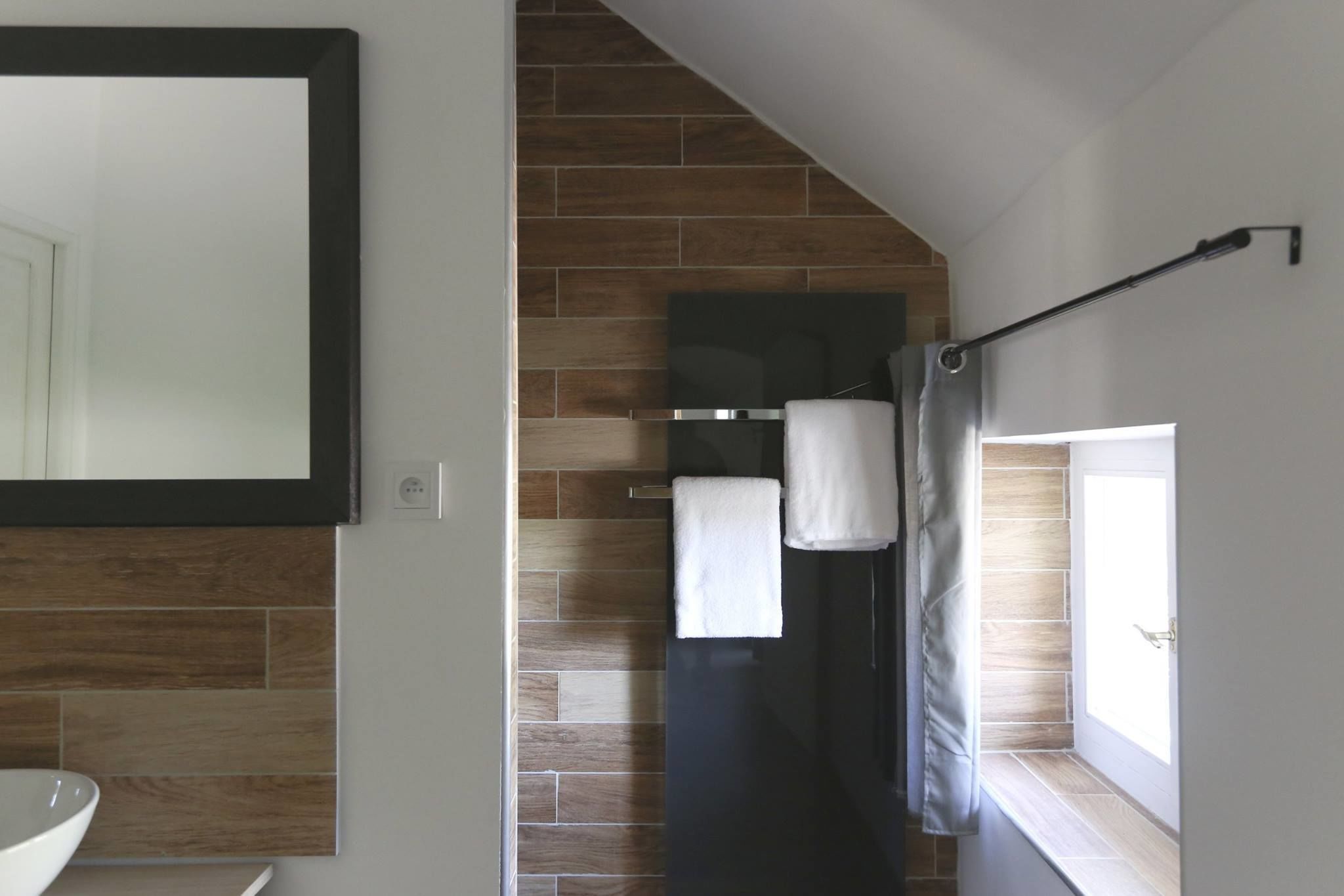 Ein Badezimmer im modernen Stil, mit einem großen Spiegel, einer Dusche mit Glastür und einem Fenster, das für natürliches Licht sorgt.