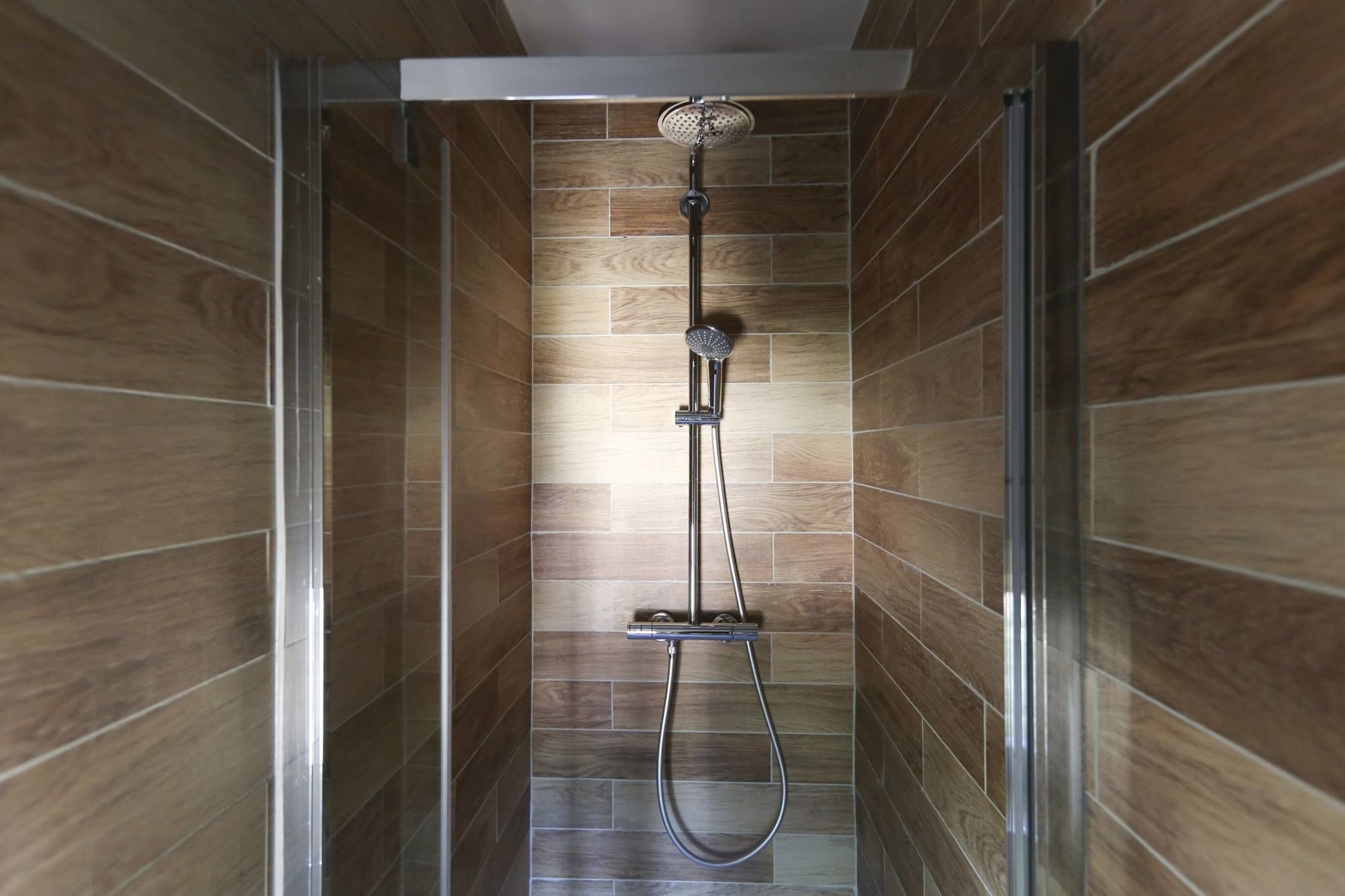 A shower with a handheld showerhead and a wall-mounted faucet, set in a room with wooden paneling.