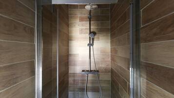 A shower with a handheld showerhead and a wall-mounted faucet, set in a room with wooden paneling.