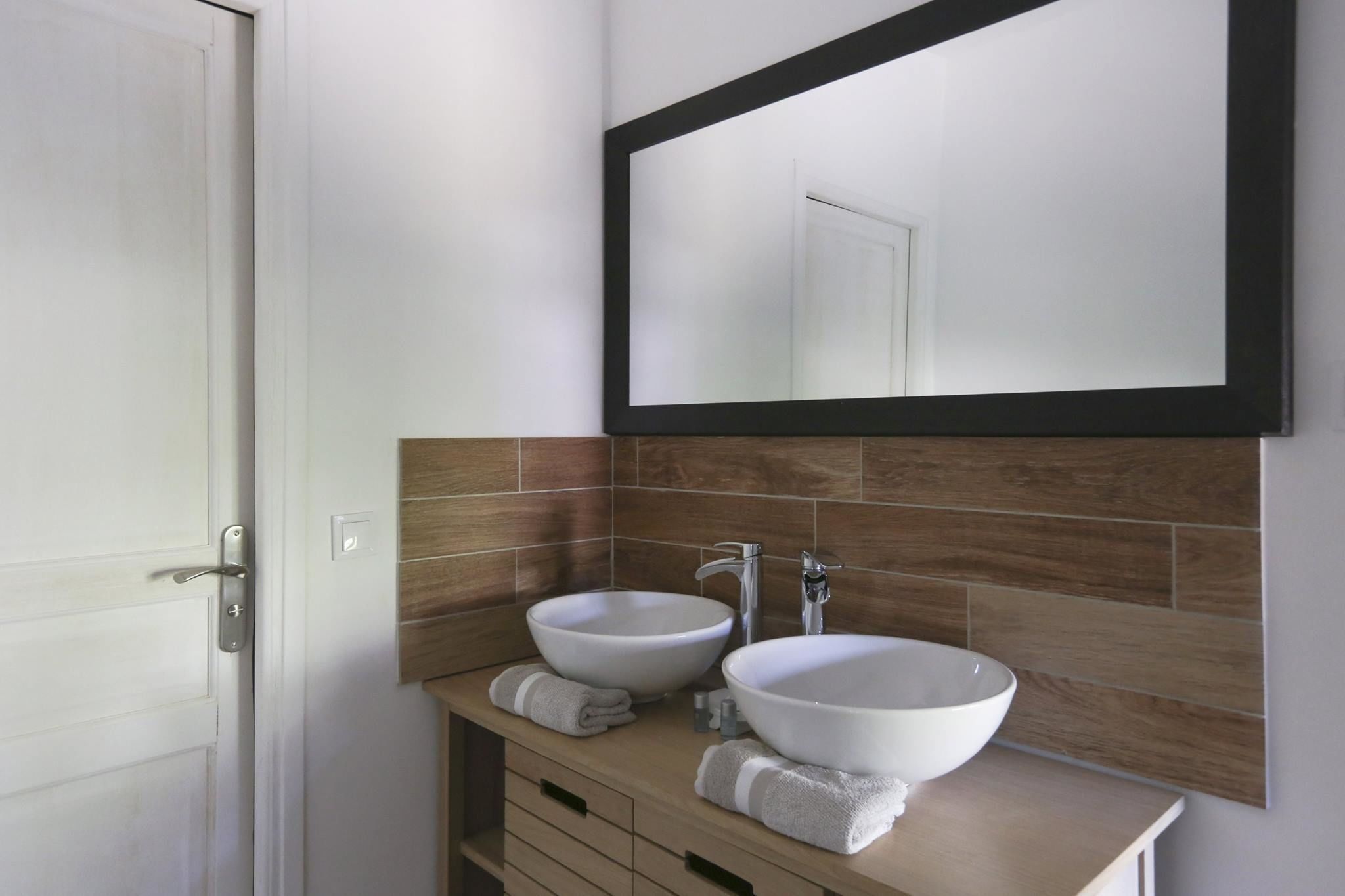 Un baño con dos lavamanos blancos tipo sobreencimera, un espejo y un mueble de tocador de madera.